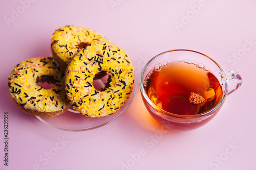 Cup of tea and yellow sweet food - doughnuts on pink table with sunshine
