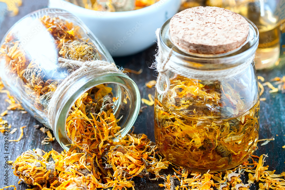 Bottles and dried calendula officinalis petals with macerated oil on wooden background.