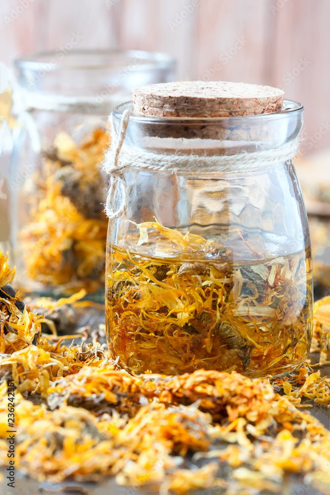 Bottles and dried calendula officinalis petals with macerated oil on wooden background.