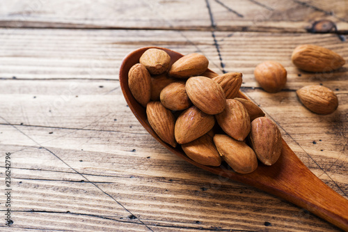 Almonds in wooden spoon on wooden background. Copy space.