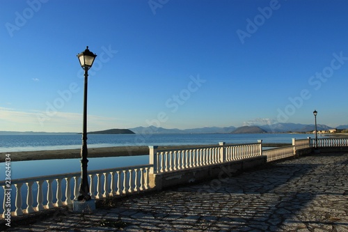 View of the Ambracian gulf from square of Koronisia village horizon and sea behind the concrete retro fence made of cement lamps in the foreground and shadows on the square paved with stones in Greece photo