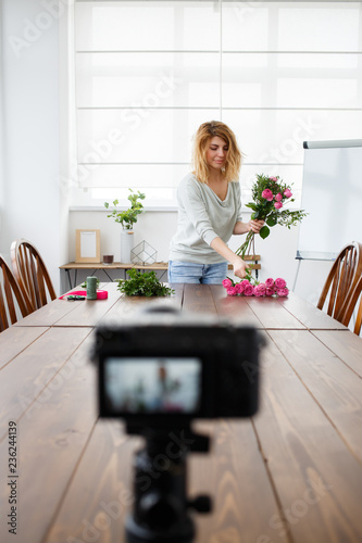 Photo of young woman florist composing bouquet of pink flowers.