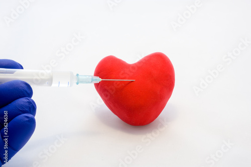 Injection into heart or cardiovascular disease treatment concept photo. Doctor holds in his hand, dressed in glove, syringe with medication and is preparing to make injection in shape card red heart photo