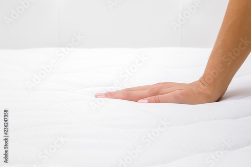 Woman's hand pressing on white mattress. Checking hardness and softness. Choice of the best type and quality. Side view. Close up. photo