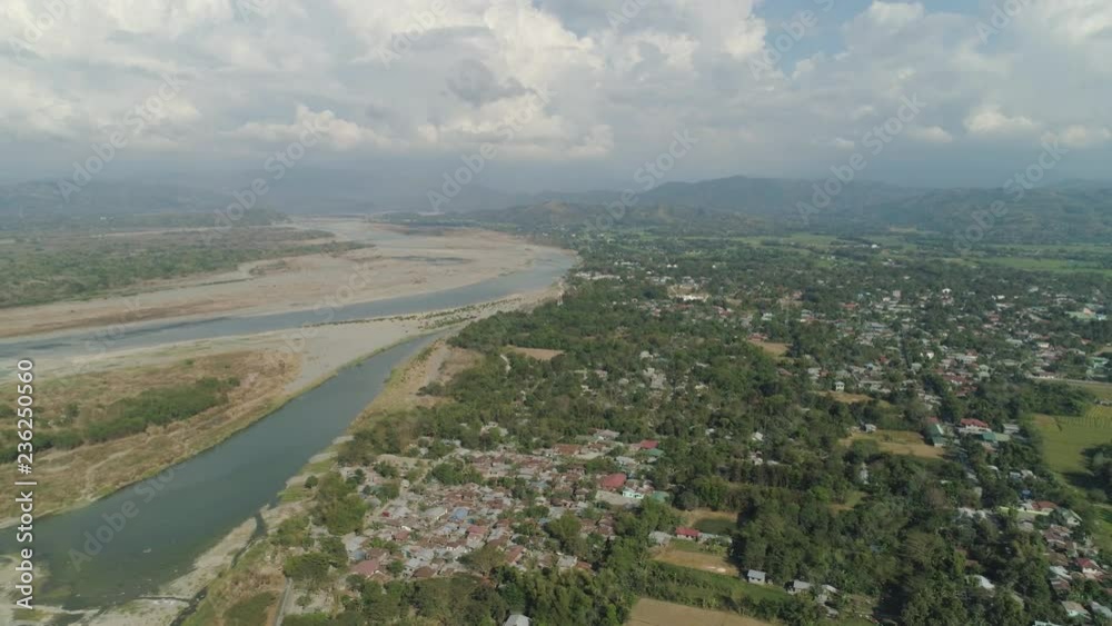 Aerial view of Farmer fields, river, village in the background of mountains on the island of Luzon, Philippines. Mountain landscape with valley and village.