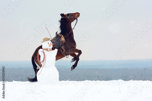 Big snowman in cowbot hat training rearing horse. Funny nordic action: rearing stallion in hand. photo