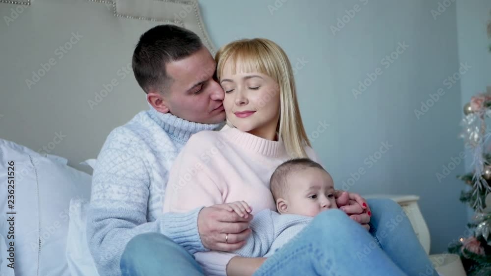 both parents are sitting on a bed with a small son a child in a blue sweater both parents are sitting on a bed with a small son a child in a blue sweater