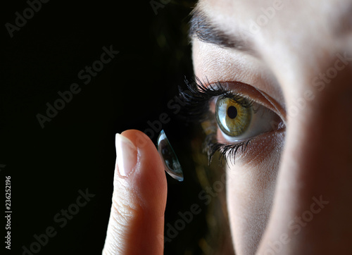 Girl putting contact lens in her eye on black background,close up.
