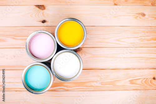 Four open cans of paint on wooden natural background. Yellow, white, pink, turquoise colors. Top view.