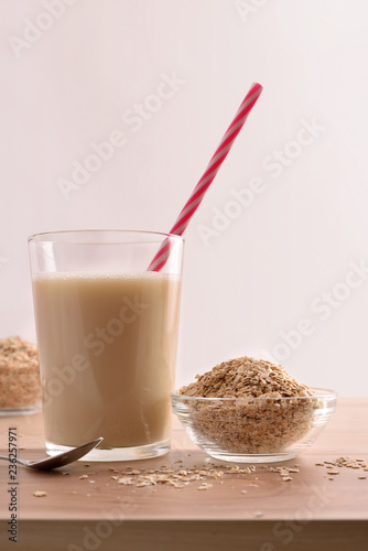 Oat drink in glass and cereal flakes white background vertical