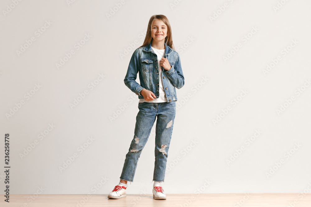 Full length portrait of cute little teen girl in stylish jeans clothes  looking at camera and smiling against white studio wall. Kids fashion  concept Stock Photo