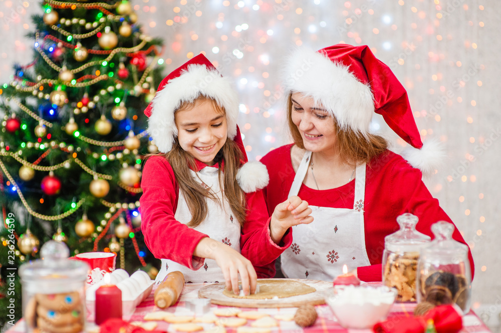 Merry Christmas and Happy Holidays. Mom and daughter in a Christmas hat are preparing a festive treat Merry Christmas and Happy Holidays. Mom and daughter in a Christmas hat are preparing a festive treat