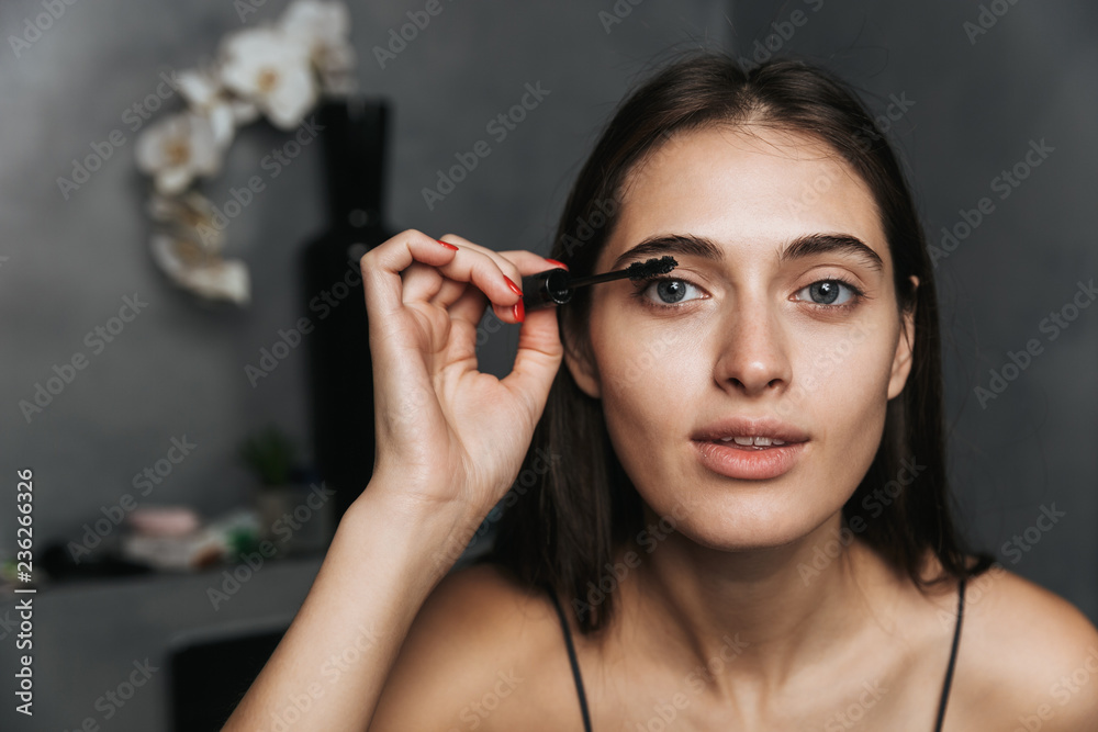 Obraz premium Cheerful cute young beautiful woman in bathroom take care of her skin doing makeup.