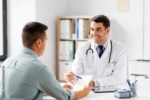 medicine, healthcare and people concept - happy smiling doctor showing prescription to patient at medical office in hospital