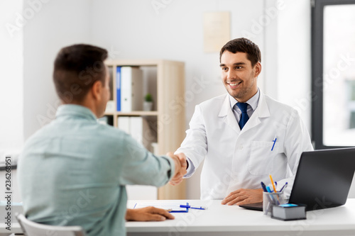 medicine, healthcare and people concept - smiling doctor and male patient shaking hands at hospital
