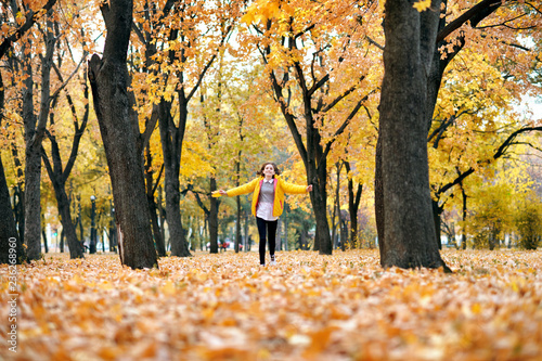 Happy teen girl is running in autumn park with big maple's leaf. Bright yellow leaves and trees.