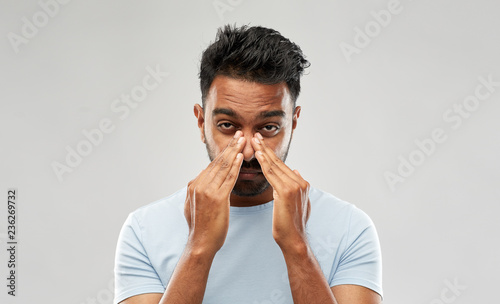 health problem and people concept - indian man rubbing nose over grey background