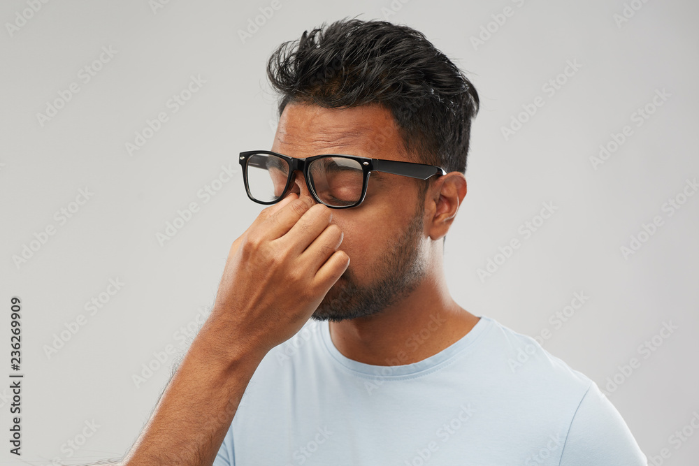 people, vision and overwork concept - tired indian man in glasses rubbing nose bridge over grey background people, vision and overwork concept - tired indian man in glasses rubbing nose bridge over grey background