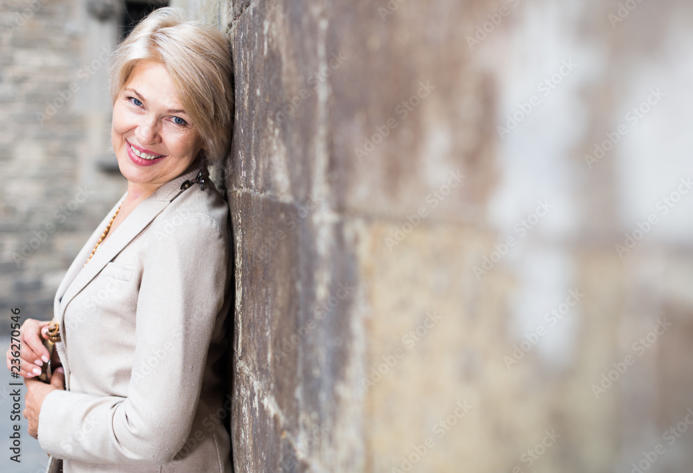Cheerful mature female is playfully posing near wall