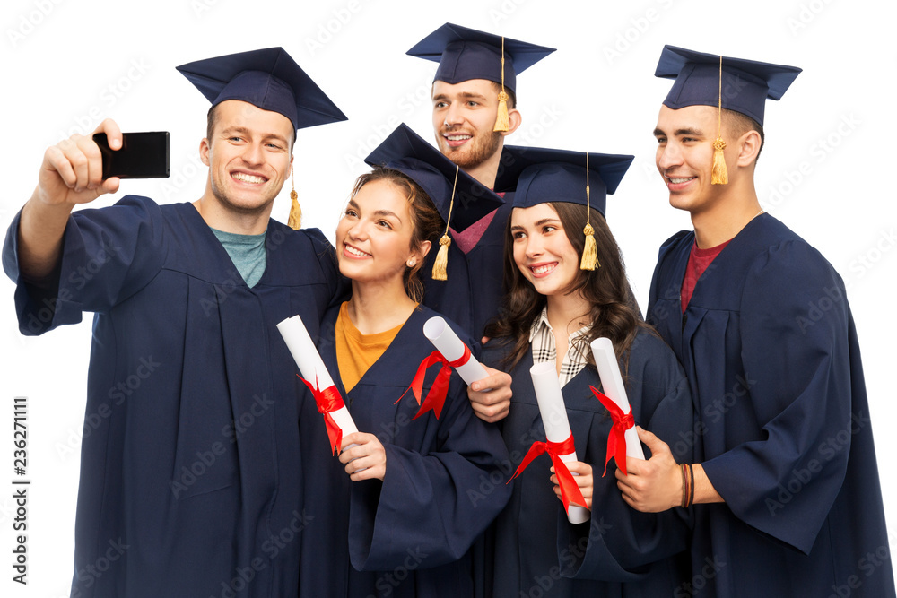 education, graduation and people concept - group of happy graduate students in mortar boards and bachelor gowns with diplomas taking selfie by smartphone over white background education, graduation and people concept - group of happy graduate students in mortar boards and bachelor gowns with diplomas taking selfie by smartphone over white background