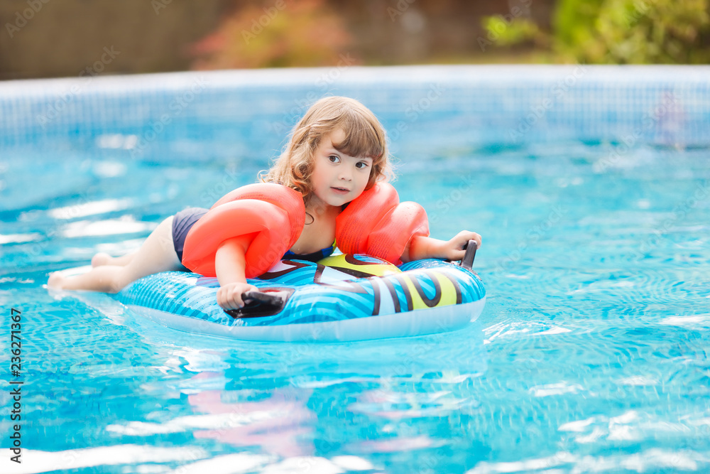 Adorable little girl with inflatable over-sleeves floats swiming in the pool, lying at the