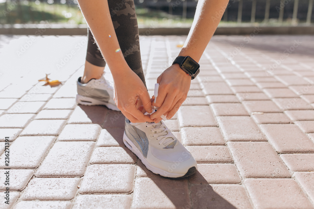 Closeup image of an athlete female tying up her laces on a bench at the park. She's bent down and wearing sport coach on her hand. Smart watch aside Closeup image of an athlete female tying up her laces on a bench at the park. She's bent down and wearing sport coach on her hand. Smart watch aside