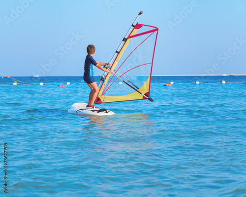 One child learning to windsurf in the open sea waters at beautiful sunset light, close up, windsurfing passtime and school with copy space