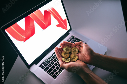 Top view of hands holding bit coins. On computer screen red arrow pointing down. photo