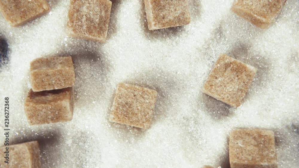 The rotation of the cubes of refined sugar brown sugar scattered on a pile of white crystalline sugar top view The rotation of the cubes of refined sugar brown sugar scattered on a pile of white crystalline sugar top view