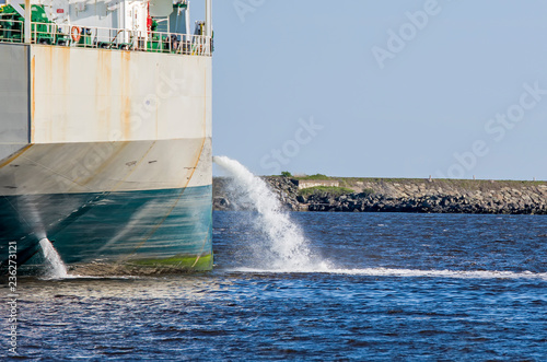Tanker discharging ballast into the harbor. Water flows from the side. Ship not identifiable. Only part of ship visible.