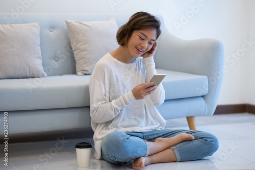 Joyful Asian girl having video call. Beautiful young woman sitting on floor in front of couch and using phone. Communication concept