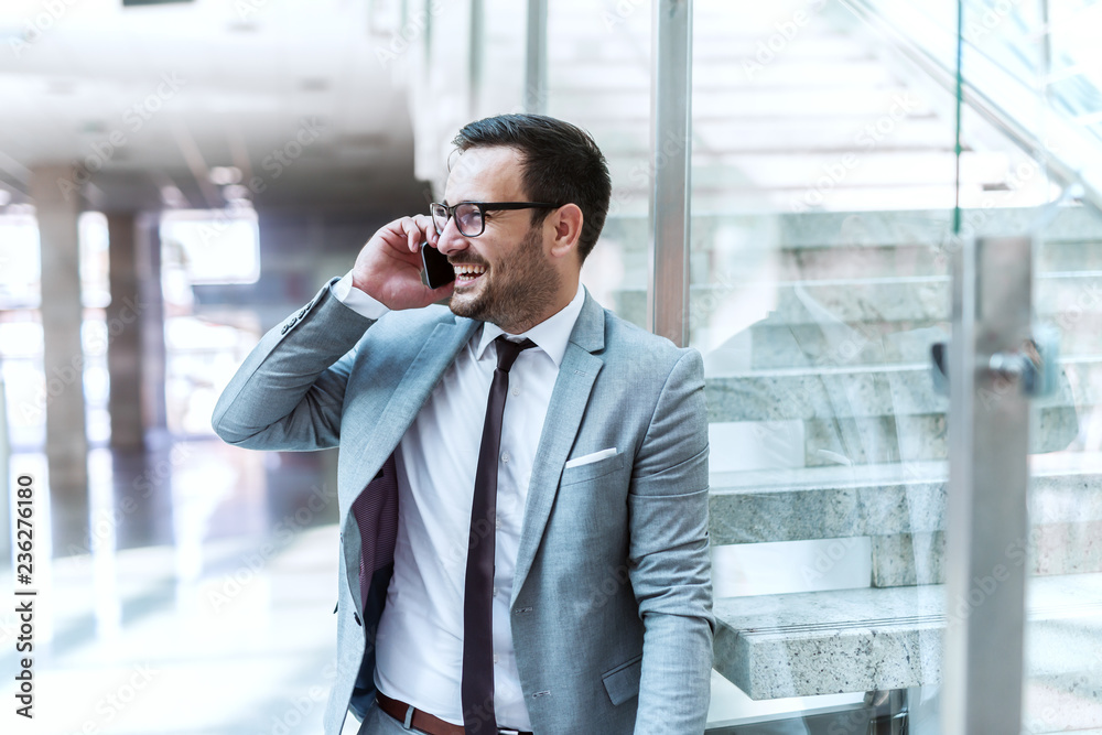 Happy suited businessman using smart phone for business talk while leaning on the glass. Happy suited businessman using smart phone for business talk while leaning on the glass.