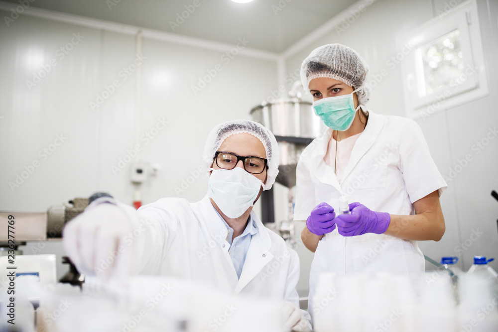 Scientist doing quality control for cosmetics while his assistant helping him. Protective suit, gloves and masks on. Scientist doing quality control for cosmetics while his assistant helping him. Protective suit, gloves and masks on.