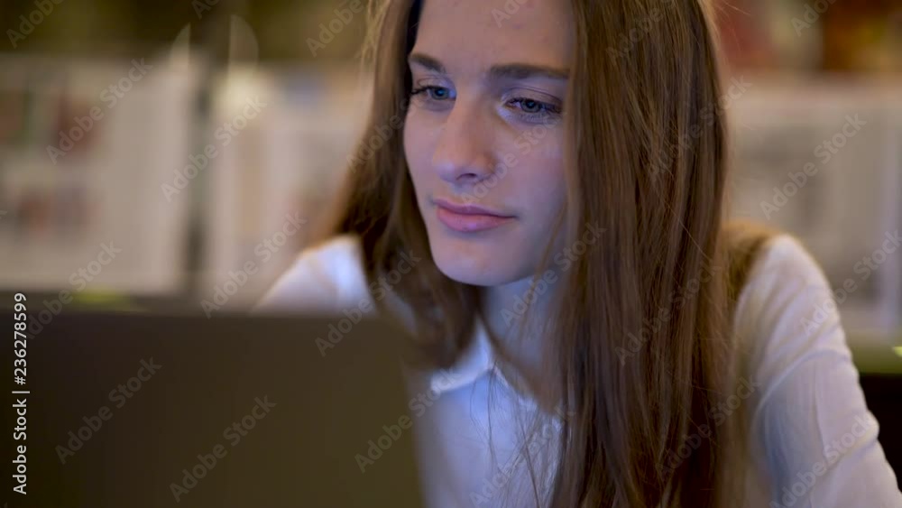A young girl sits in a cafe and talking on the phone, typing on a laptop, drinking tea. Business girl. A young girl sits in a cafe and talking on the phone, typing on a laptop, drinking tea. Business girl.