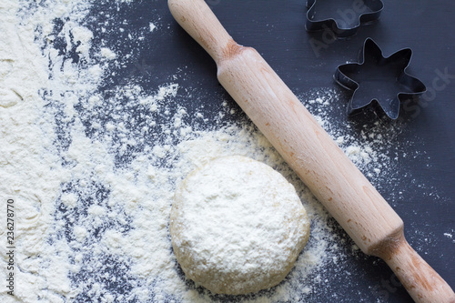 fresh raw pastry dough, rolling pin and cookie cutters on dark background