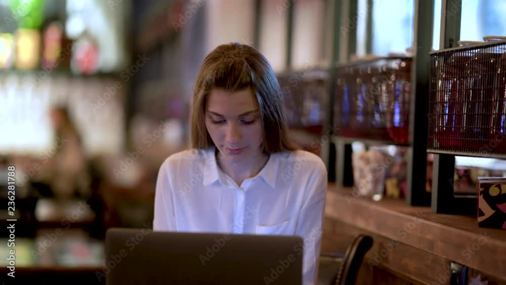 A young girl sits in a cafe and talking on the phone, typing on a laptop, drinking tea. Business girl. A young girl sits in a cafe and talking on the phone, typing on a laptop, drinking tea. Business girl.
