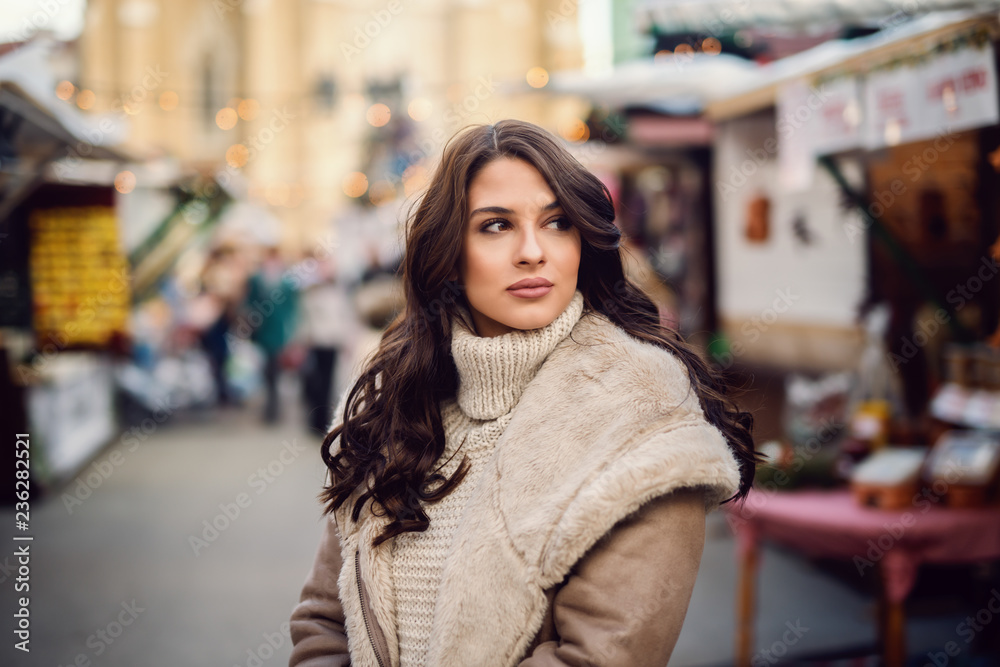 Beautiful Caucasian brunette in coat standing on the street and looking away.
