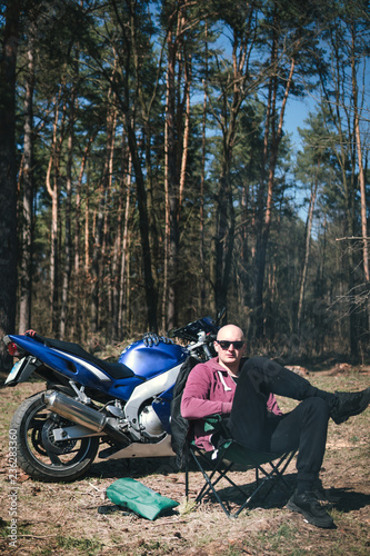 man near campfire enjoying summer day in forest. off road motorcycle, enduro bike, biker resting outdoors, vertical photo