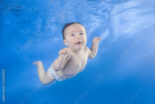 Funny face portrait of little baby girl swimming and diving underwater with fun in pool  on a blue water background.  