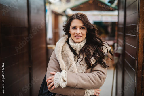 Gorgeous Caucasian woman in coat standing on the street on cold weather with crossed arms.