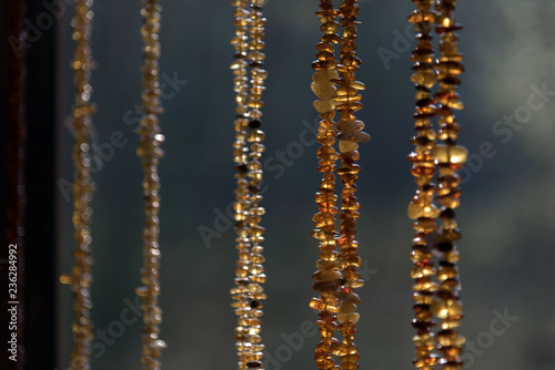 Beads from amber hang parallel to each other on a blurred background. Some. Day. Sunlight makes amber magical, glowing from the inside.