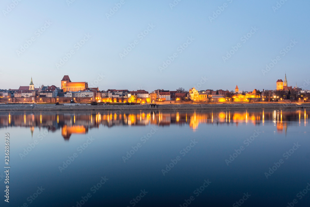 TORUN, POLAND - panorama of the Old Town district, listed as one of UNESCO World Heritage Sites, with picturesque night illuminations and evening sky water reflections.