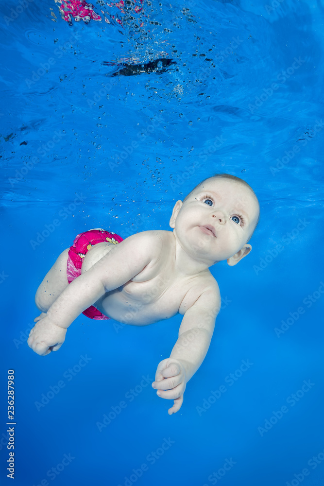 Beautiful baby girl swim underwater on blue water background. Healthy family lifestyle and children water sports activity. Child development, disease prevention