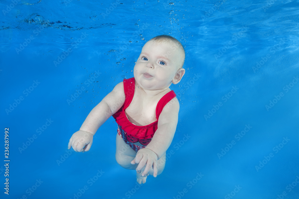 Beautiful baby girl in a red swimming suit swim underwater on blue water background. Healthy family lifestyle and children water sports activity. Child development, disease prevention