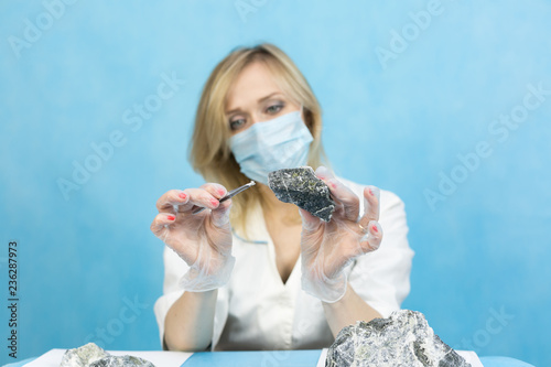 The girl laboratory technician examines samples of minerals. A woman lab worker examines the stones with tweezers takes the fibers of harmful asbestos.