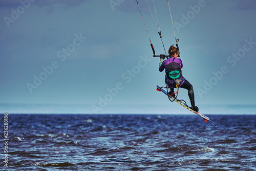 A female kiter jumps over a large lake.