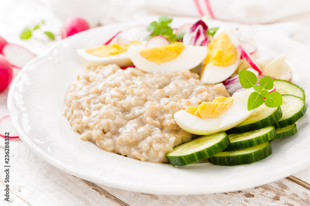 Oatmeal porridge with boiled egg and vegetable salad with fresh radish, cucumber and lettuce. Healthy dietary breakfast