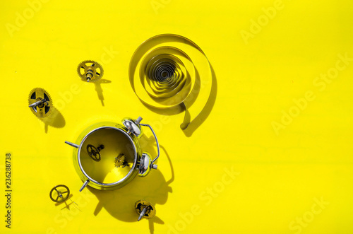 Old alarm clock disassembled into gears on a bright yellow background with hard shadows.