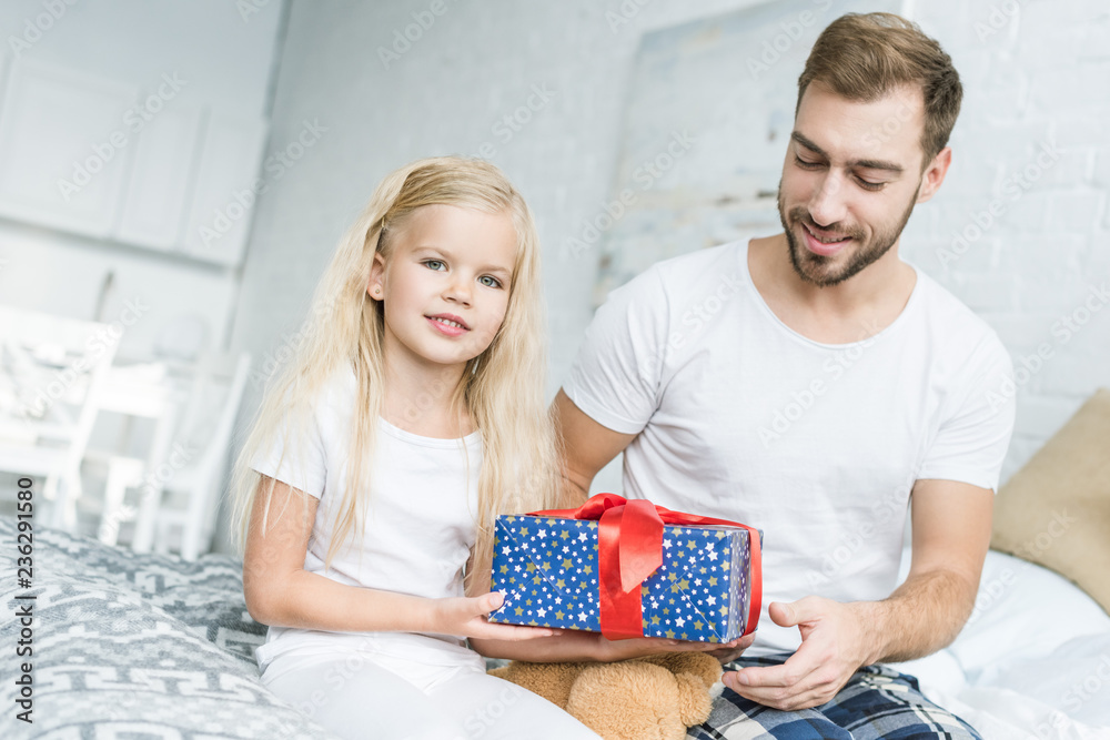 happy father looking at cute little daughter holding gift box at home happy father looking at cute little daughter holding gift box at home