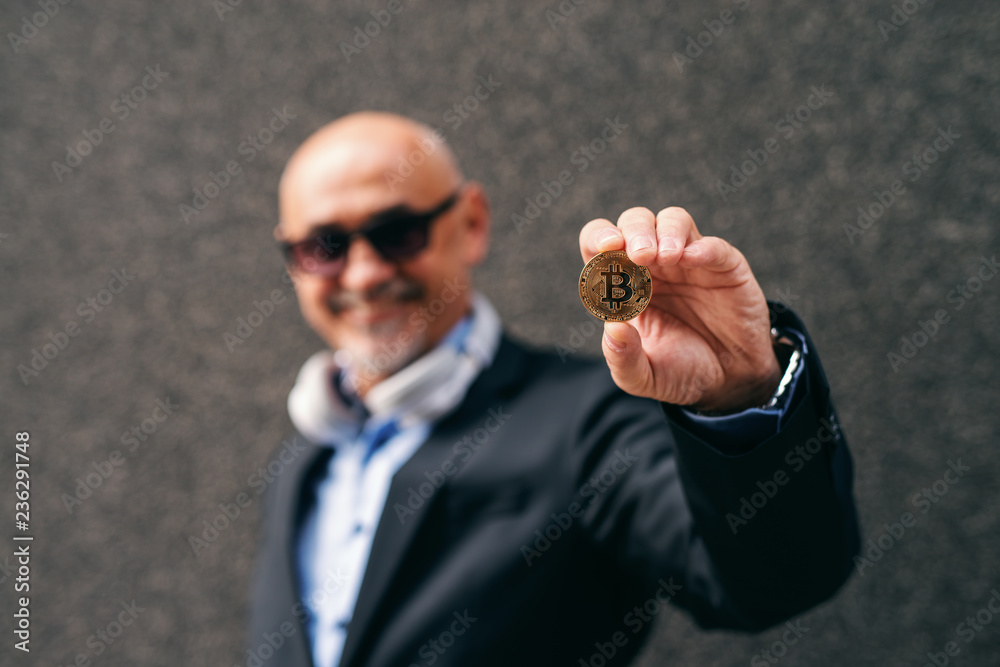 Fototapeta premium Bearded senior adult wealthy businessman holding bit-coin. Selective focus on bit-coin.